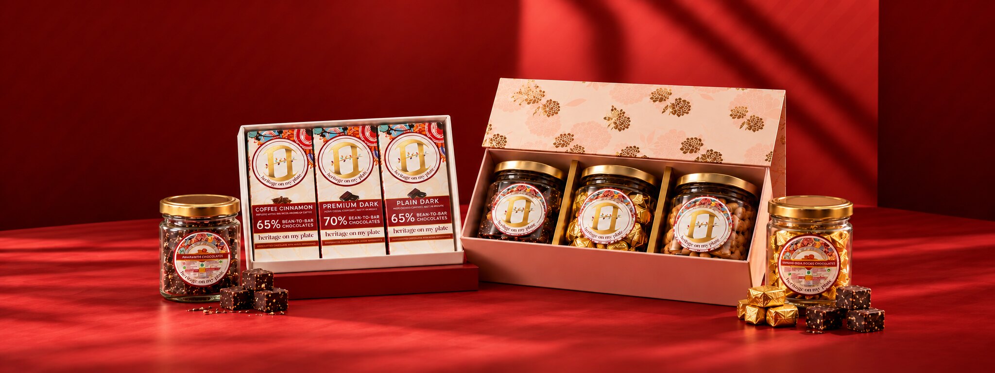 Heritage On My Plate gift boxes on a crimson set: three bean to bar chocolates in one, three jars of chocolates in a floral box, with amaranth and Shining Gold Rocks jars beside them